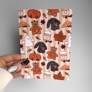 May include: A rectangular sticker sheet featuring a repeating pattern of autumn-themed illustrations on a light tan and white striped background. The design includes smiling pumpkins, brown teddy bears, black bunnies, white ghosts, coffee cups, and leaves.