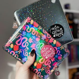May include: Two phone cases, one clear with a glittery black design and the other with a colorful floral and snake pattern. Both cases have the text "Hot Girls Read". Each case has a charm attached.