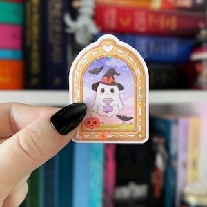 May include: A Halloween-themed sticker featuring a cartoon ghost wearing a witch hat and holding a potion. The sticker is framed with a gold border and includes bats and a pumpkin. The background is a colorful, blurred image of books.