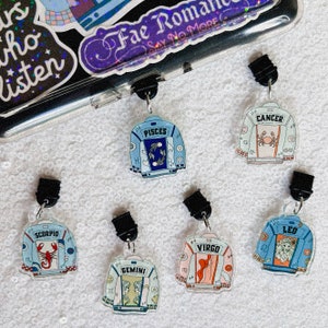 May include: Six different zodiac sign charms, each featuring a denim jacket design with a zodiac symbol and astrological details. The charms are attached to black metal rings.
