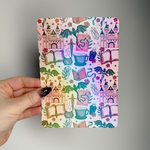 May include: A rectangular sticker with a repeating pattern of castles, books, potion bottles, bats, and crystals. The design has a rainbow gradient background with pink, yellow, green, and blue hues. The sticker is held by a hand.