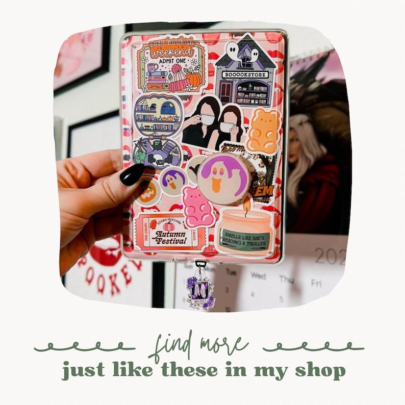 May include: A pink and white planner with a variety of stickers, including a ghost, a gummy bear, and a book store. The planner has a calendar with the month of October and the year 2022. The planner has a charm attached to it with the letter M.