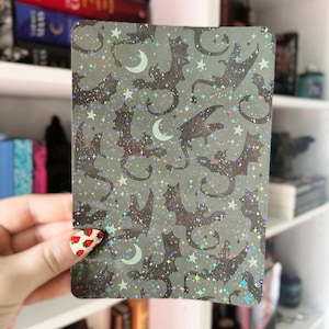 May include: A holographic card with a repeating pattern of black silhouettes of dragons, stars, and crescent moons on a gray background.