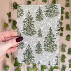 May include: A sheet of decorative paper with a repeating pattern of green Christmas trees on a white background with a subtle sparkle effect.