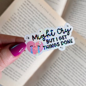 May include: A white sticker with a glittery pink heart with a crying face and the text "Might cry but I get things done" in black.