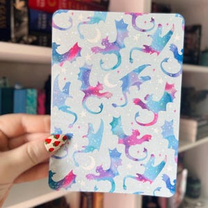 May include: A blue and purple patterned sticker with a repeating design of watercolor dragons. The dragons are silhouetted against a light blue background with white stars and moons.