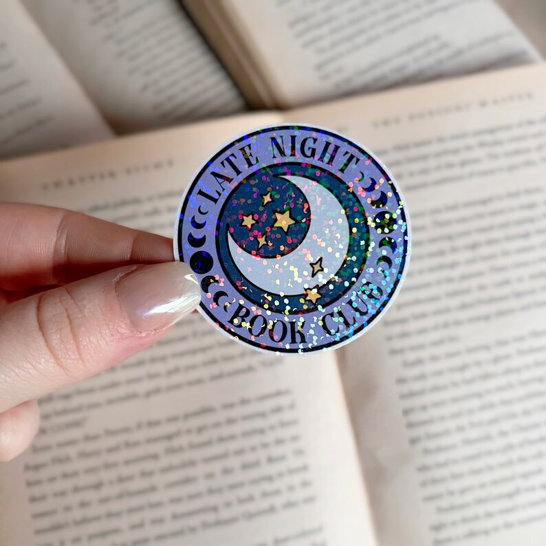 May include: A round sticker with a crescent moon and stars on a purple background. The text "Late Night Book Club" is written around the moon and stars.