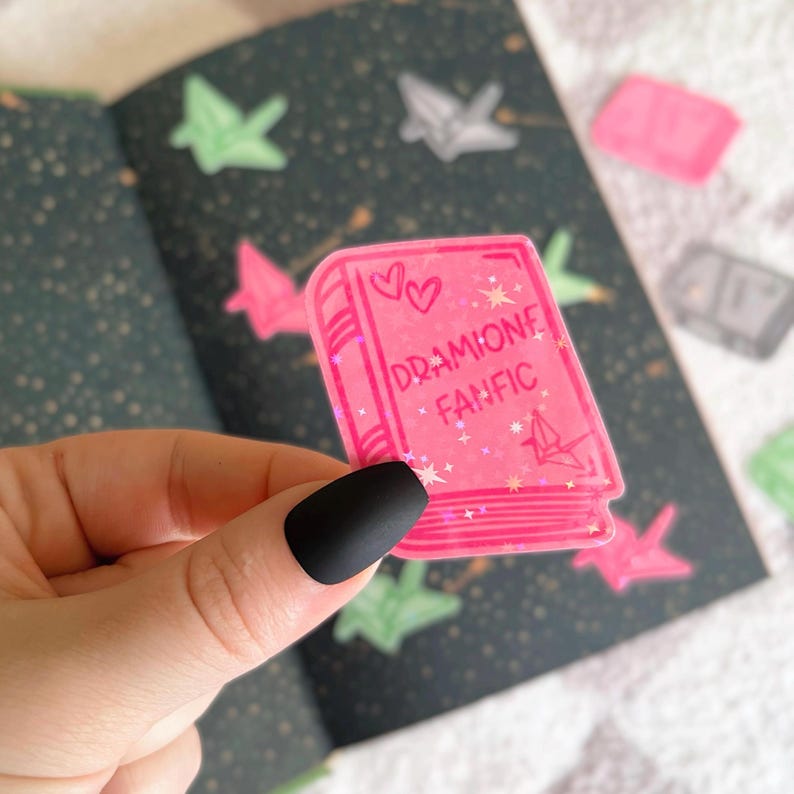 May include: Pink book-shaped sticker with glitter and the text "DRAMIIONE FANFIC" and two hearts.