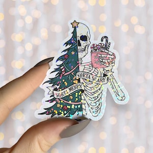 May include: A glittery sticker featuring a skeleton dressed as a Christmas tree holding a mug of hot cocoa. The text "Sorta Merry" and "Sorta Scary" is written on the sticker.
