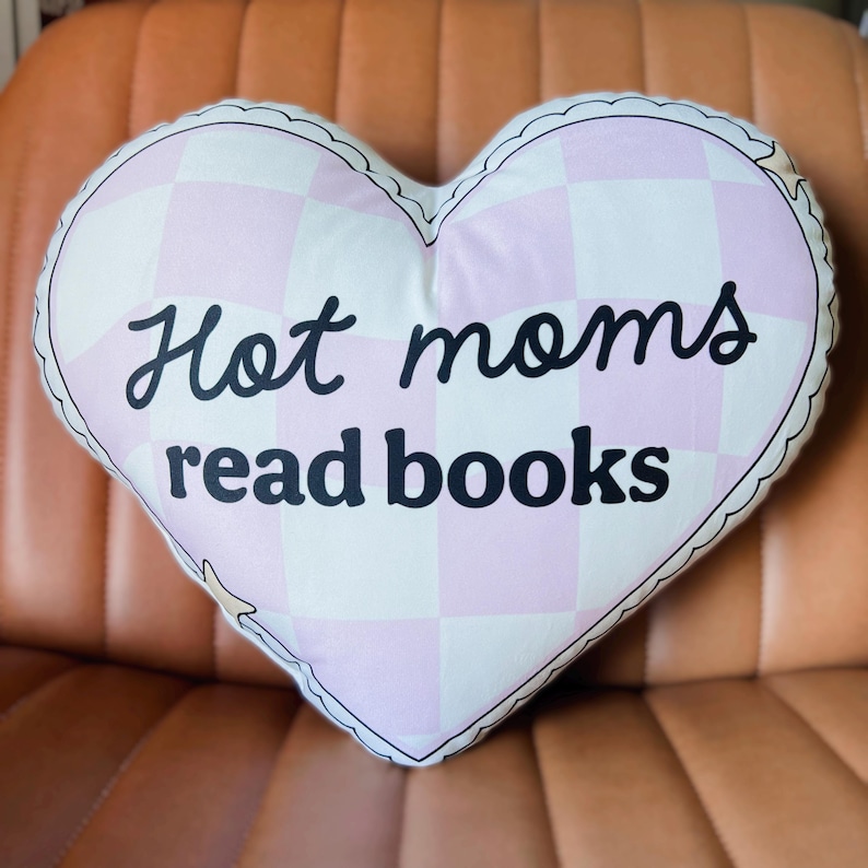 May include: A pink and white heart-shaped pillow with the text "Hot moms read books" in black.