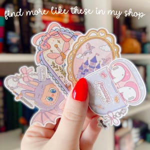 Puede incluir: Una colecci&oacute;n de pegatinas caprichosas con ilustraciones en tonos pastel. Los dise&ntilde;os incluyen un castillo de cuento de hadas, una lib&eacute;lula, un conejito con disfraz de murci&eacute;lago y una funda con auriculares. El texto "Fantasy Audiogirl" es visible.