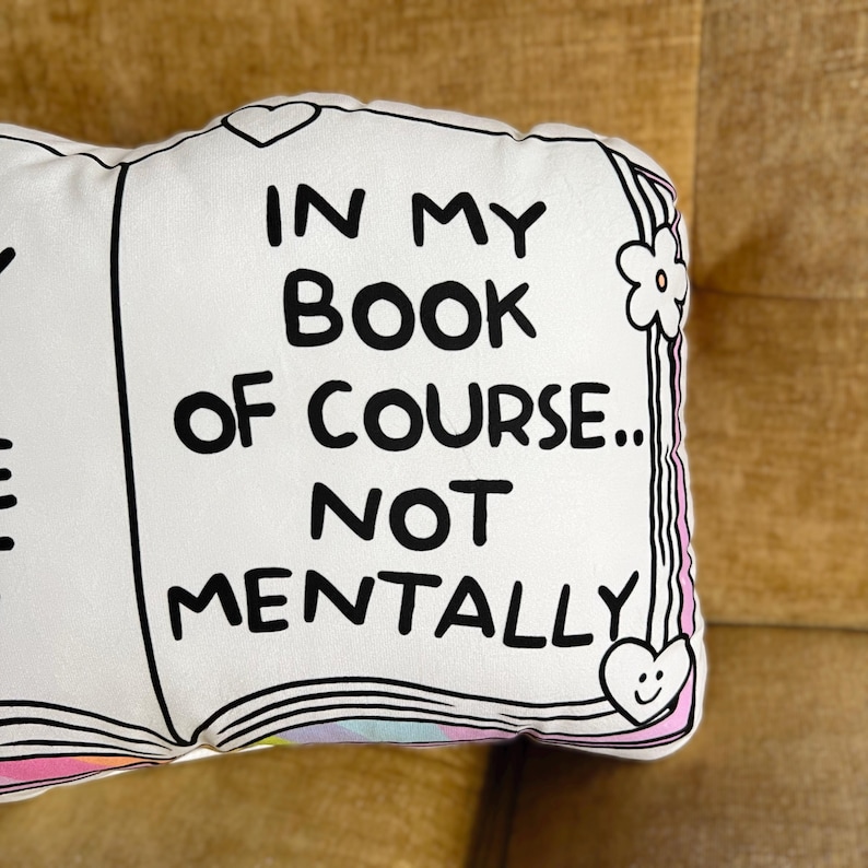 May include: White pillow with black text that reads "In my book of course... not mentally". The pillow is shaped like an open book with a pink and white design on the edges.