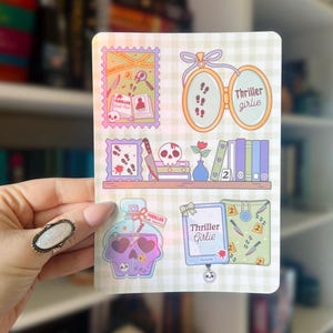 May include: A sticker sheet featuring various illustrations with a thriller theme. Designs include a skull, footprints, a knife, a perfume bottle, and the text "Thriller Girlie". The background is a light green and white checkered pattern.