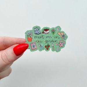 Peut inclure: Un autocollant vert avec le texte "meet me in the garden" et des illustrations sur le th&egrave;me du jardin. L'autocollant pr&eacute;sente des images d'un pot de fleurs, de bottes, de fraises, de fleurs, d'un chapeau, d'un arrosoir, d'un paquet de graines, de cisailles, de tomates et d'une truelle.