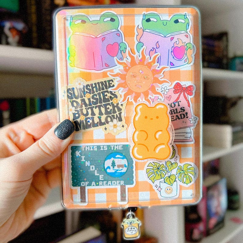 Pu&ograve; includere: Una copertina per planner in plastica trasparente con una variet&agrave; di adesivi colorati, tra cui un sole, un orsacchiotto gommoso, rane che leggono libri e un cartello che dice "Questo &egrave; il Kindle di un lettore".
