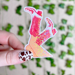May include: A sticker of a pair of legs in pink cowboy boots with glitter accents. The boots are crossed at the ankles and the legs are sparkly.