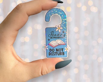 May include: A blue glittery door hanger with the text "Reading in progress" and "Do not disturb". The door hanger features an open book illustration and small white flowers.