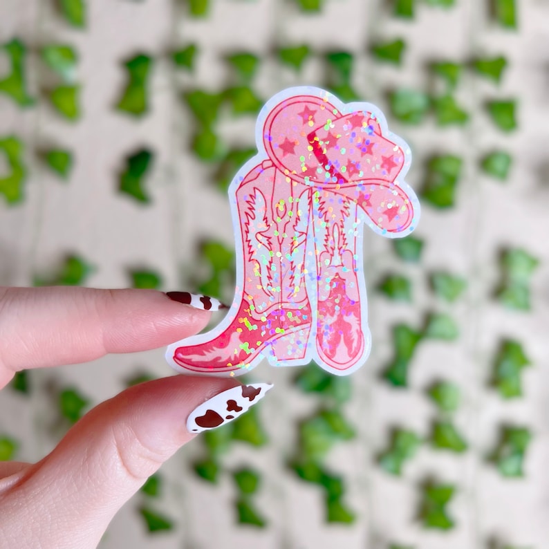 May include: Pink glitter cowboy boots and a pink glitter cowboy hat sticker. The sticker is on a white background.