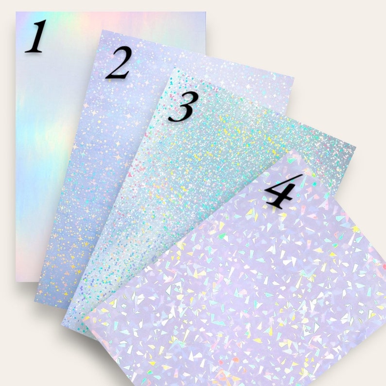 May include: Four sheets of iridescent paper with different patterns. The first sheet has a rainbow gradient, the second has a white background with small blue and silver glitter, the third has a white background with small blue, green, and silver glitter, and the fourth has a white background with small blue, green, and silver glitter in a geometric pattern.