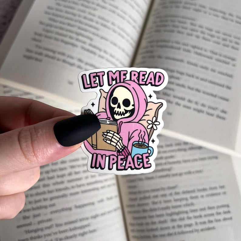 May include: A pink and white sticker with a skeleton wearing a pink hoodie and holding a book. The sticker says "Let me read in peace".