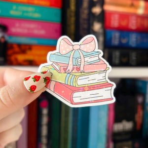May include: A stack of five books with a pink bow on top. The books are decorated with glitter and hearts. The books are stacked on a white surface.