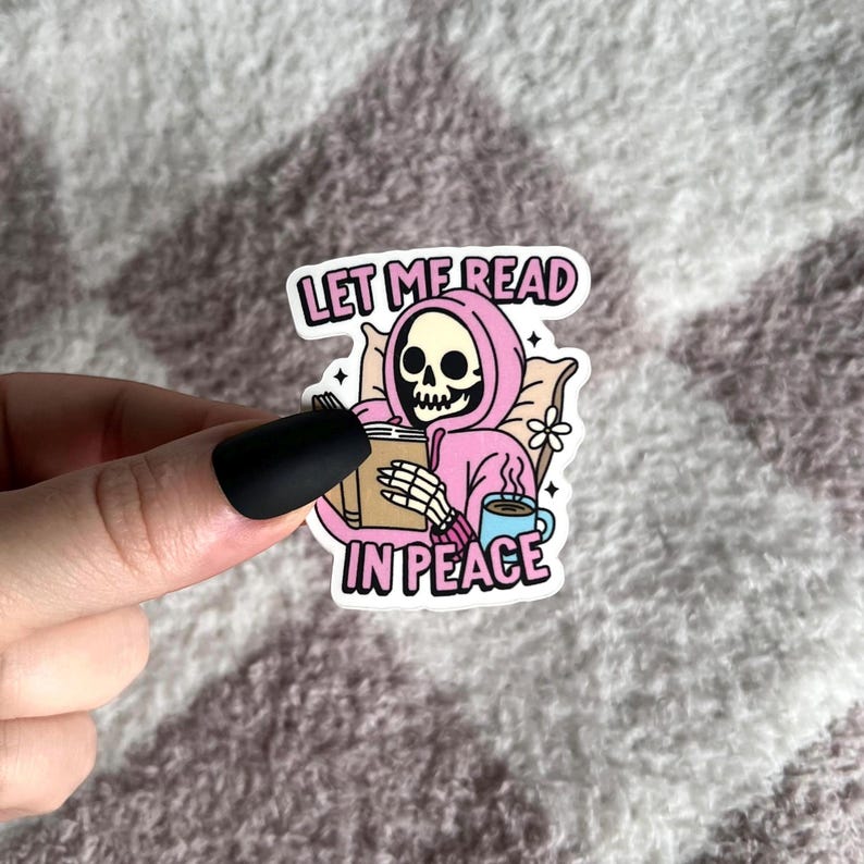 May include: A pink and white sticker with a skeleton wearing a pink hoodie and holding a book. The text on the sticker reads "Let me read in peace".