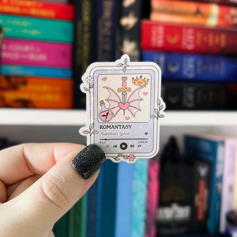 May include: A pink and purple sticker with a glittery background. The sticker features a cartoon illustration of a heart, a sword, a crown, and a potion bottle. The sticker also includes the text "ROMANTASY Audiobook Series" and a play button.