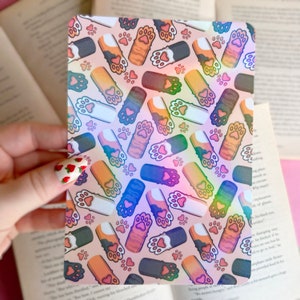 May include: A holographic sticker with a repeating pattern of colorful cat paw prints on a pink background.