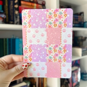 May include: A pink and purple patchwork card with a peace sign pattern. The card has a glittery finish.