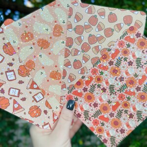 Puede incluir: Cuatro hojas de papel con diferentes patrones y un acabado brillante. Los patrones incluyen calabazas, fantasmas, maíz dulce y diseños de otoño.