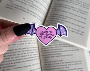 May include: A pink heart-shaped sticker with purple bat wings. The sticker has the text "I like my men tall, dark & Illyrian" on it.