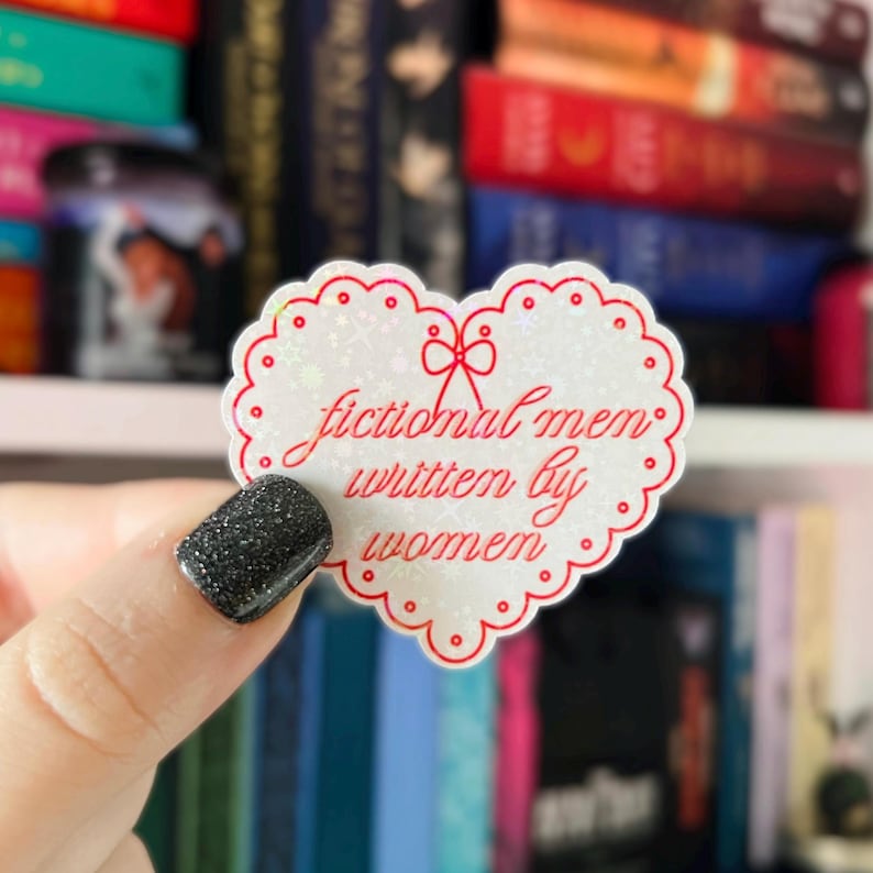 May include: A white heart-shaped sticker with a red glitter outline and red text that reads "fictional men written by women".
