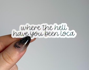 May include: A die-cut sticker with a holographic finish featuring the black text "where the hell have you been loca" in a cursive script font. The sticker has a white border and a shimmering, reflective surface that catches the light.