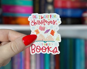May include: A colorful sticker with the text "All I Want For Christmas Is More Books" in red and white. The sticker features illustrations of open books, snowflakes, and a Christmas tree. The background is a blurred image of books.