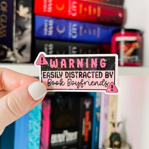May include: A pink and black warning sticker with glitter accents. The sticker reads "WARNING EASILY DISTRACTED BY Book Boyfriends!"