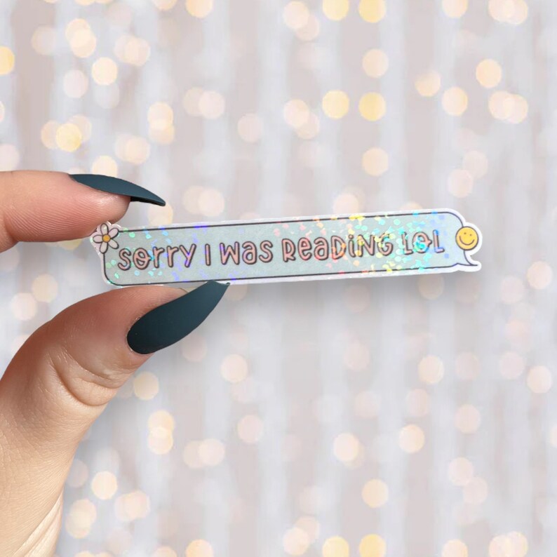 Op de afbeelding: Een holografische sticker met een blauwe achtergrond en een witte rand. De sticker heeft een tekstballon met de tekst "sorry i was reading lol" en een klein smiley-gezicht.