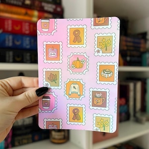 May include: A pink rectangular sticker sheet featuring various fall-themed illustrations within postage stamp borders. Designs include a coffee cup, a scarf, a pumpkin, a leaf, a sweater, a candle, and a cinnamon roll. The background has a gradient effect.