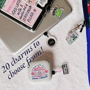 May include: A collection of 20 charms to choose from, including a charm with a local library building, a charm with the text "Mentally, I'm at the bookstore", a charm with the text "smut", a charm with the text "Night Court", and a charm with a smiley face and the text "Star Night Readers Club".