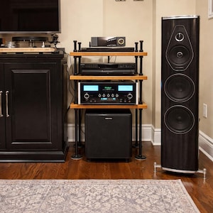 May include: A home entertainment system featuring a tall, dark wood-grain speaker and a multi-tiered audio rack. The rack holds various components, including a receiver, CD player, and a subwoofer. The setup is on a hardwood floor.