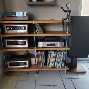 May include: A wooden audio rack with multiple shelves holding stereo equipment, including a turntable, receiver, and cassette deck. The rack also displays vinyl records and a black speaker. A decorative metal figure sits on top.