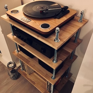 May include: A wooden audio rack with an AKAI turntable on top. The rack has four shelves, with a black amplifier and other audio components. The shelves are supported by metal rods and bolts. A vinyl record is on the turntable.