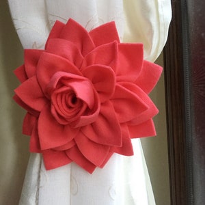 May include: A bright coral felt flower curtain tieback. The flower has a layered, rosette-like center and multiple petals.
