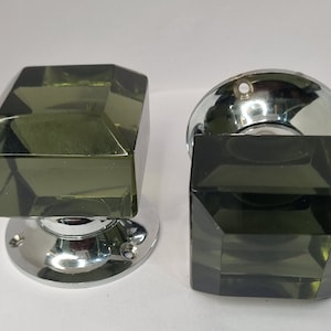 May include: Two square-shaped glass door knobs with a chrome finish. The knobs are a dark green colour.