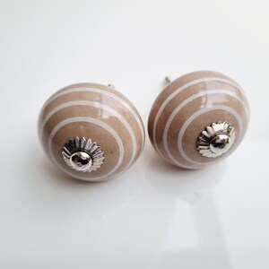 May include: Two decorative cabinet knobs. Each knob is a light brown color with white horizontal stripes. The knobs have a silver-colored, flower-shaped base. These knobs are perfect for adding a touch of style to any cabinet or drawer.