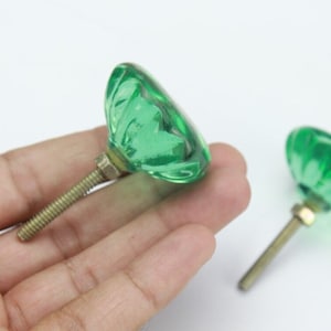 Puede incluir: Dos pomos de armario de vidrio verde con un diseño acanalado y un tornillo de latón.