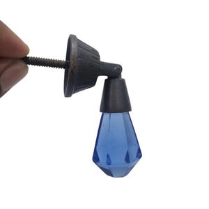 May include: A blue glass diamond-shaped knob with a metal base and screw. The knob is attached to a metal base with a screw.