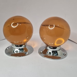 Può includere: Due pomelli per porte in vetro ambrato con basi cromate. I pomelli sono rotondi e hanno una finitura liscia e lucida.