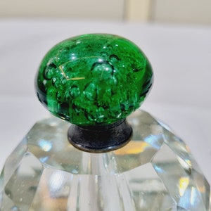 Op de afbeelding: Een groene glazen knop met luchtbellen, gemonteerd op een heldere kristallen basis. De basis heeft een facetgeslepen ontwerp.
