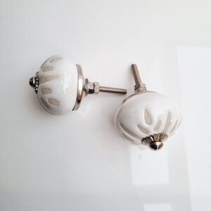 May include: Two white ceramic cabinet knobs with a floral design and silver hardware. The knobs have a rounded shape and are designed for easy installation. These decorative knobs add a touch of elegance to any furniture piece.