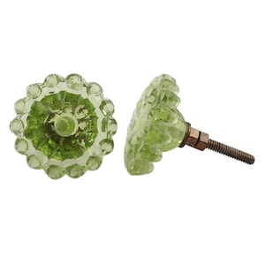 May include: Two light green glass cabinet knobs with a scalloped, flower-like edge and a faceted center. Each knob features a circular, translucent design and includes a threaded metal bolt extending from the back for attachment to furniture.